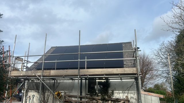 Roof with installed solar panels, surrounded by scaffolding during installation process.