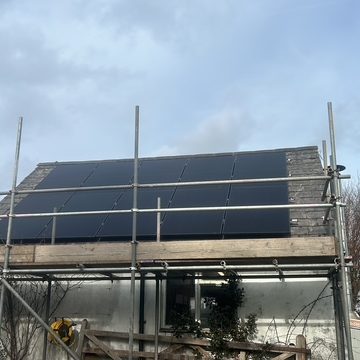 Roof with installed solar panels, surrounded by scaffolding during installation process.